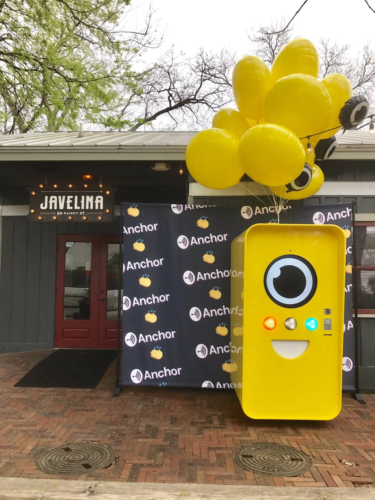 Yellow Snapbot vending machine with balloons in front of an Anchor step-and-repeat outside Javelina bar on Rainey Street